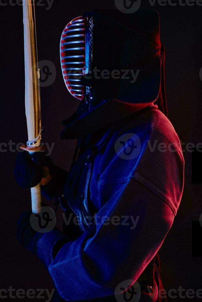 cerca arriba disparo, kendo combatiente vistiendo en un armadura, tradicional kimono, casco practicando marcial Arte con shinai bambú espada, negro antecedentes. foto