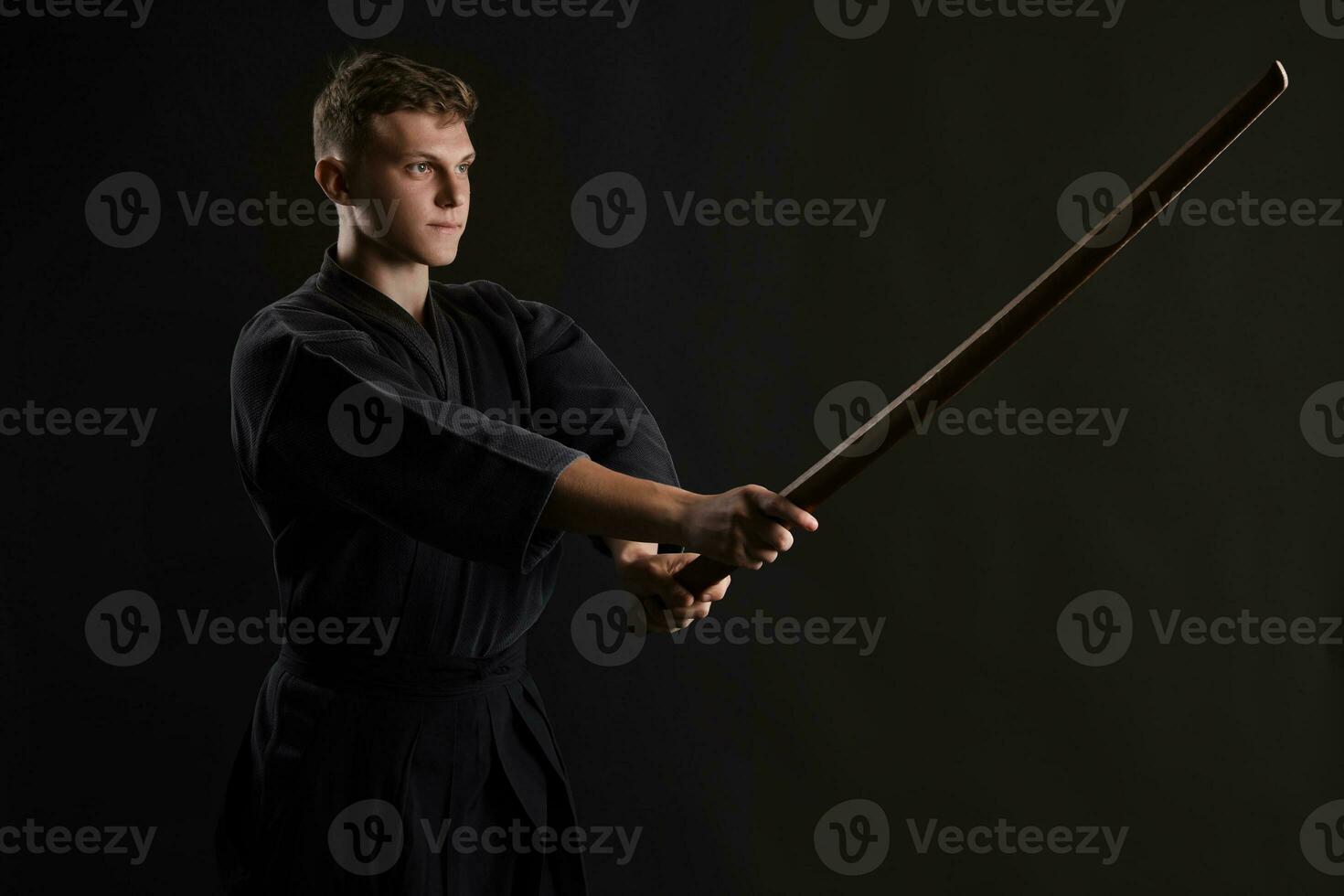 Kendo guru wearing in a traditional japanese kimono is practicing martial art with the shinai bamboo sword against a black studio background. photo