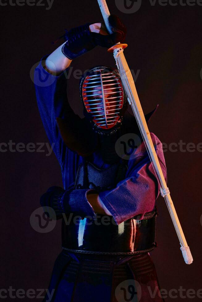Close up shot, Kendo fighter wearing in an armor, traditional kimono, helmet practicing martial art with shinai bamboo sword, black background. photo
