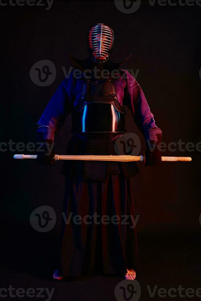 cerca arriba disparo, kendo combatiente vistiendo en un armadura, tradicional kimono, casco practicando marcial Arte con shinai bambú espada, negro antecedentes. foto