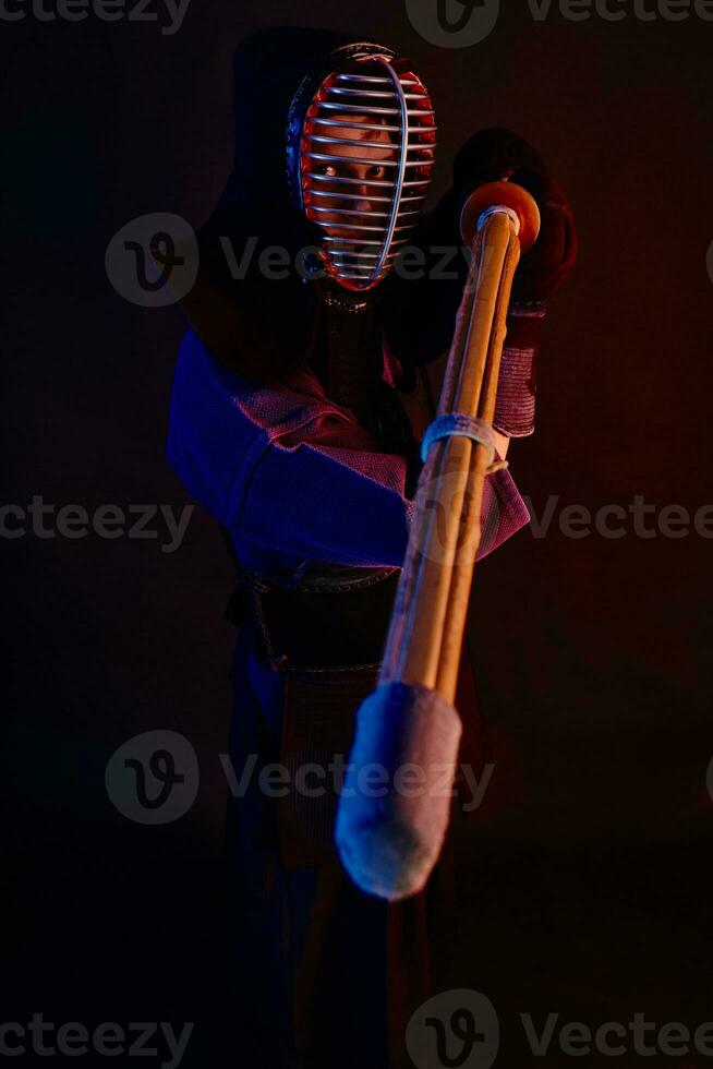 Close up shot, Kendo fighter wearing in an armor, traditional kimono, helmet practicing martial art with shinai bamboo sword, black background. photo