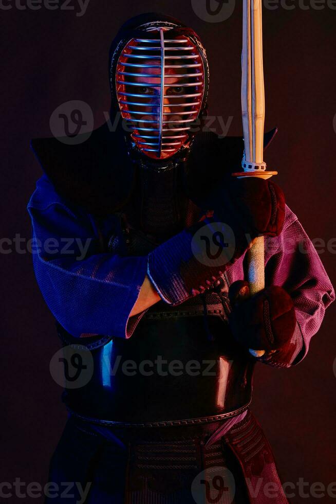 Close up shot, Kendo fighter wearing in an armor, traditional kimono, helmet practicing martial art with shinai bamboo sword, black background. photo