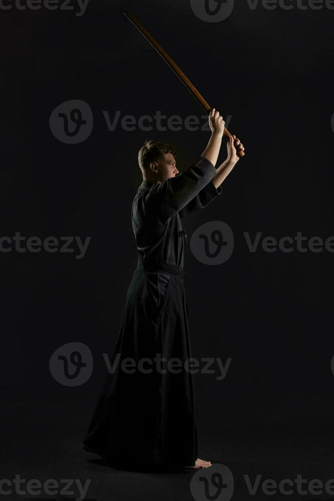 kendo gurú vistiendo en un tradicional japonés kimono es practicando marcial Arte con el shinai bambú espada en contra un negro estudio antecedentes. foto