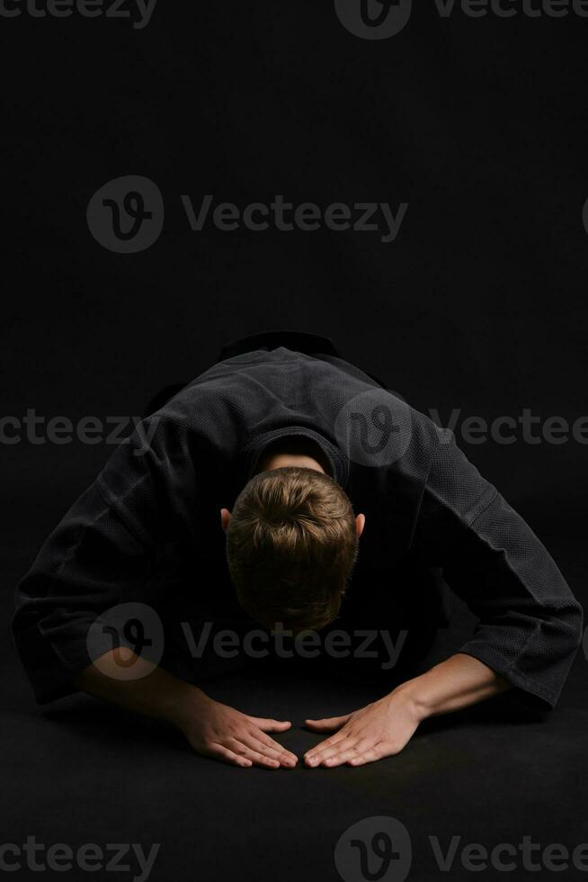 Kendo guru wearing in a traditional japanese kimono is practicing martial art with the shinai bamboo sword against a black studio background. photo