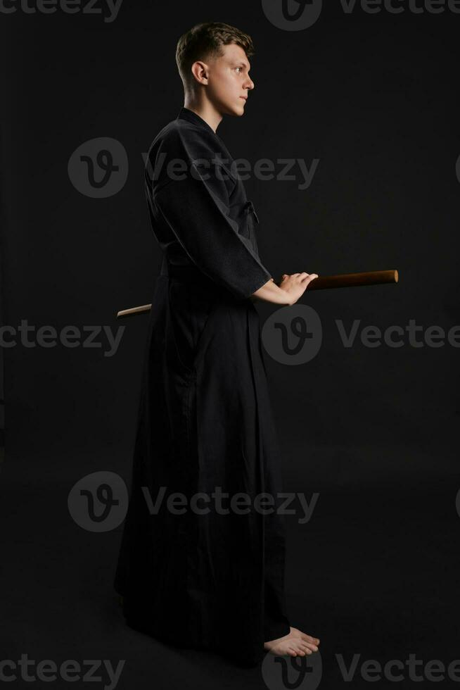 kendo gurú vistiendo en un tradicional japonés kimono es practicando marcial Arte con el shinai bambú espada en contra un negro estudio antecedentes. foto