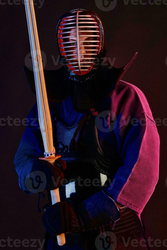 Close up shot, Kendo fighter wearing in an armor, traditional kimono, helmet practicing martial art with shinai bamboo sword, black background. photo