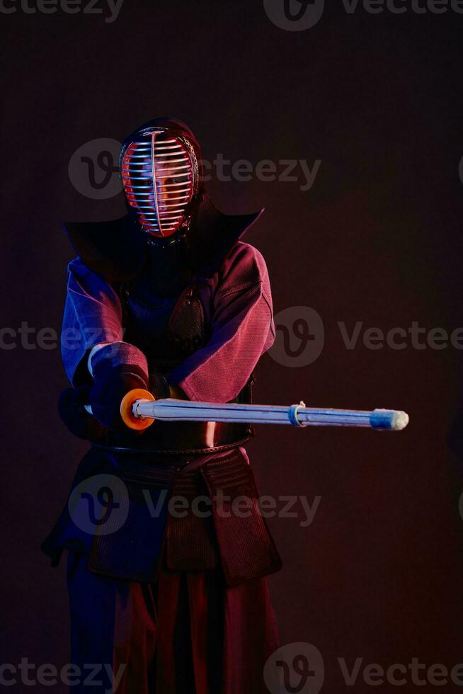 Close up shot, Kendo fighter wearing in an armor, traditional kimono, helmet practicing martial art with shinai bamboo sword, black background. photo