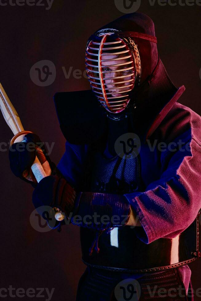 cerca arriba disparo, kendo combatiente vistiendo en un armadura, tradicional kimono, casco practicando marcial Arte con shinai bambú espada, negro antecedentes. foto