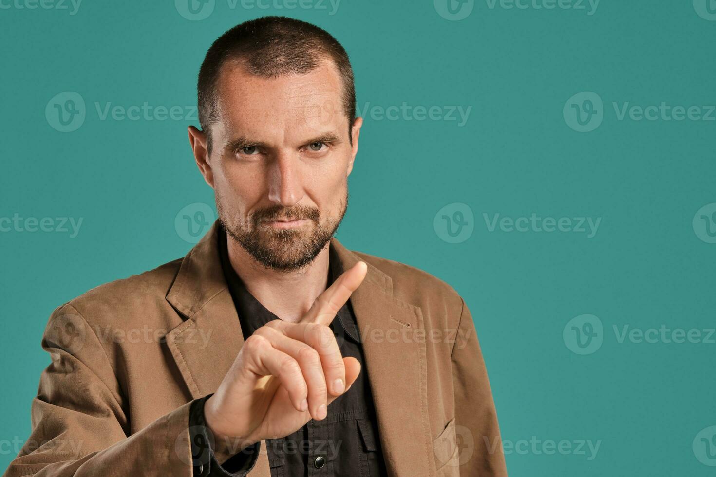 Middle-aged man with beard and mustache, wears black shirt and brown jacket posing against a blue background. Sincere emotions concept. photo