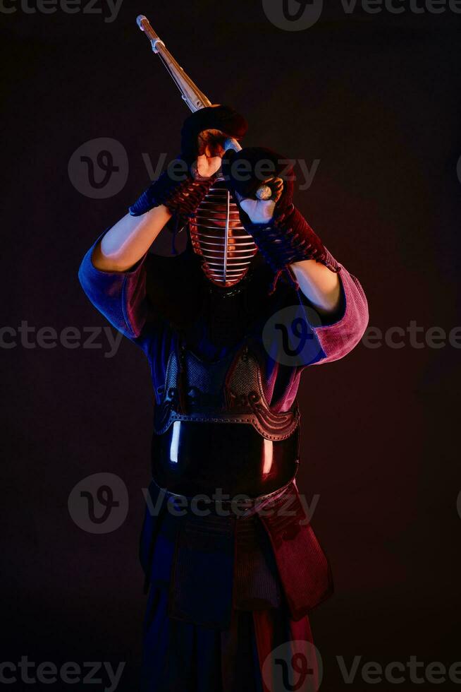 Close up shot, Kendo fighter wearing in an armor, traditional kimono, helmet practicing martial art with shinai bamboo sword, black background. photo