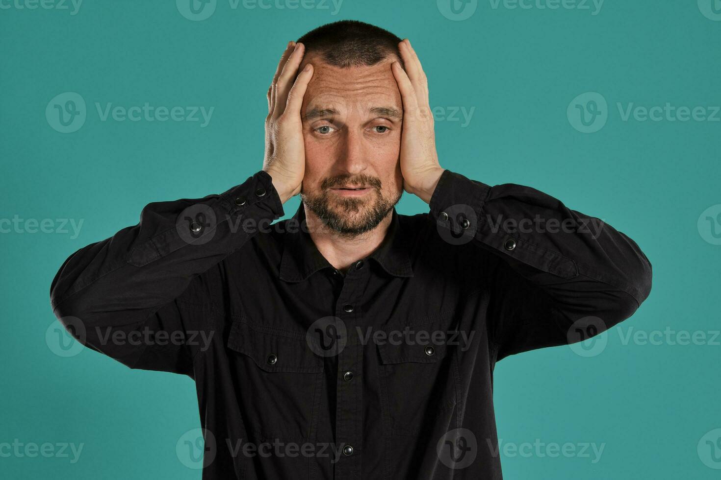 Middle-aged man with beard and mustache, wears black shirt, posing against a blue background. Sincere emotions concept. photo