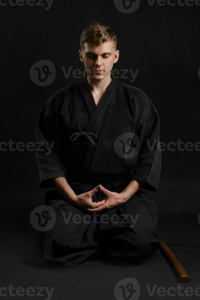 Kendo guru wearing in a traditional japanese kimono is practicing martial art with the shinai bamboo sword against a black studio background. photo