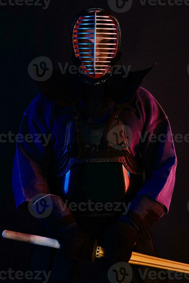 Close up shot, Kendo fighter wearing in an armor, traditional kimono, helmet practicing martial art with shinai bamboo sword, black background. photo