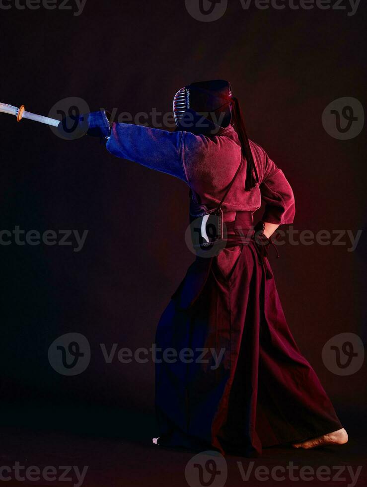 cerca arriba disparo, kendo combatiente vistiendo en un armadura, tradicional kimono, casco practicando marcial Arte con shinai bambú espada, negro antecedentes. foto