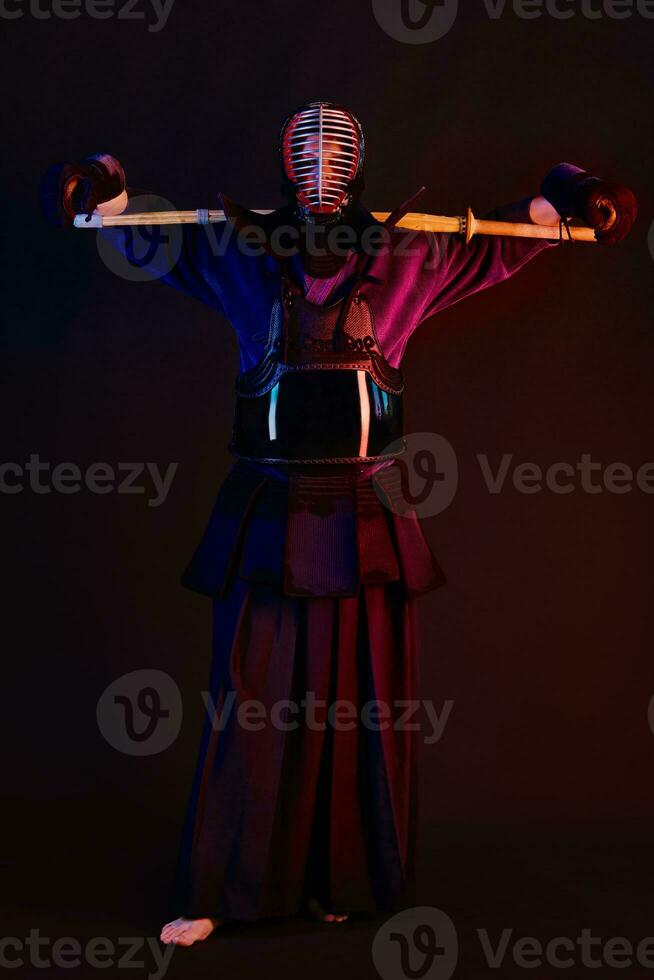 Close up shot, Kendo fighter wearing in an armor, traditional kimono, helmet practicing martial art with shinai bamboo sword, black background. photo