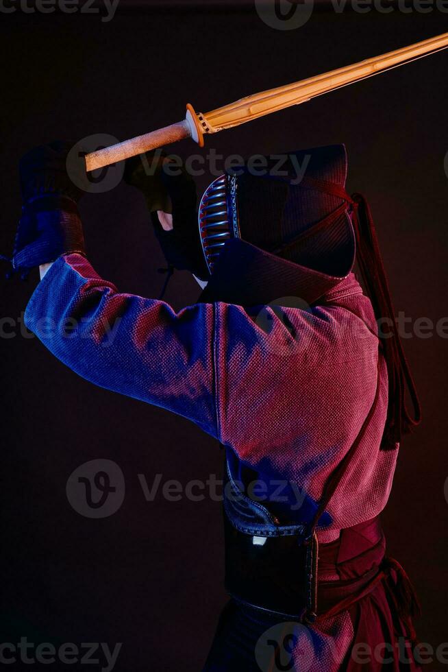 Close up shot, Kendo fighter wearing in an armor, traditional kimono, helmet practicing martial art with shinai bamboo sword, black background. photo