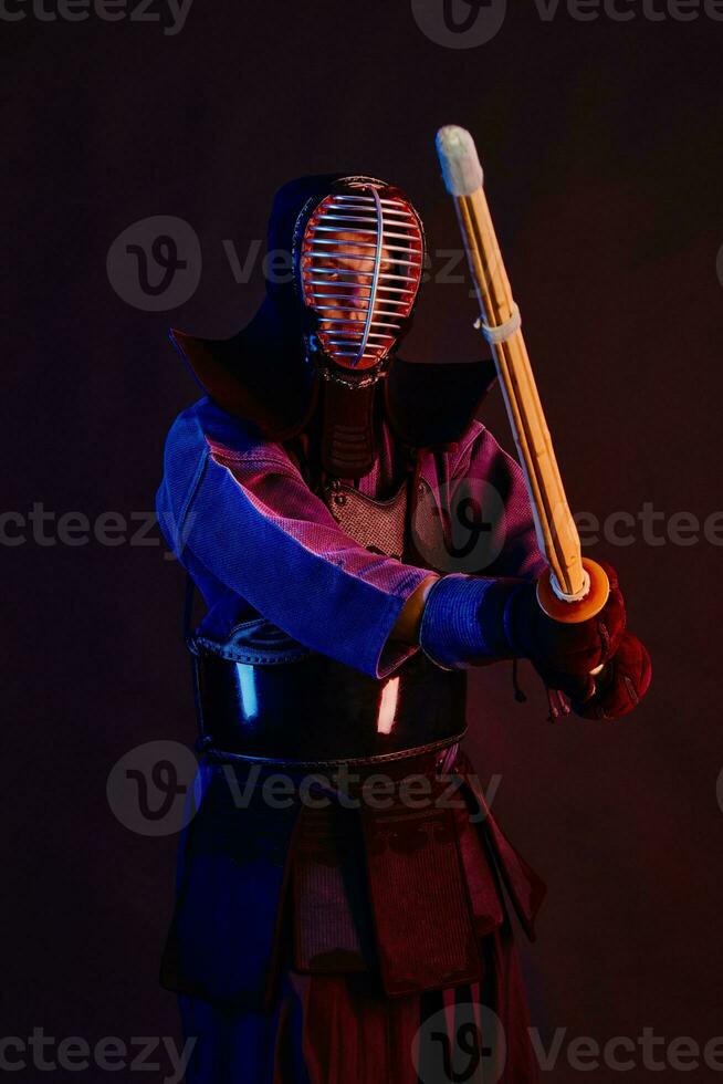 Close up shot, Kendo fighter wearing in an armor, traditional kimono, helmet practicing martial art with shinai bamboo sword, black background. photo