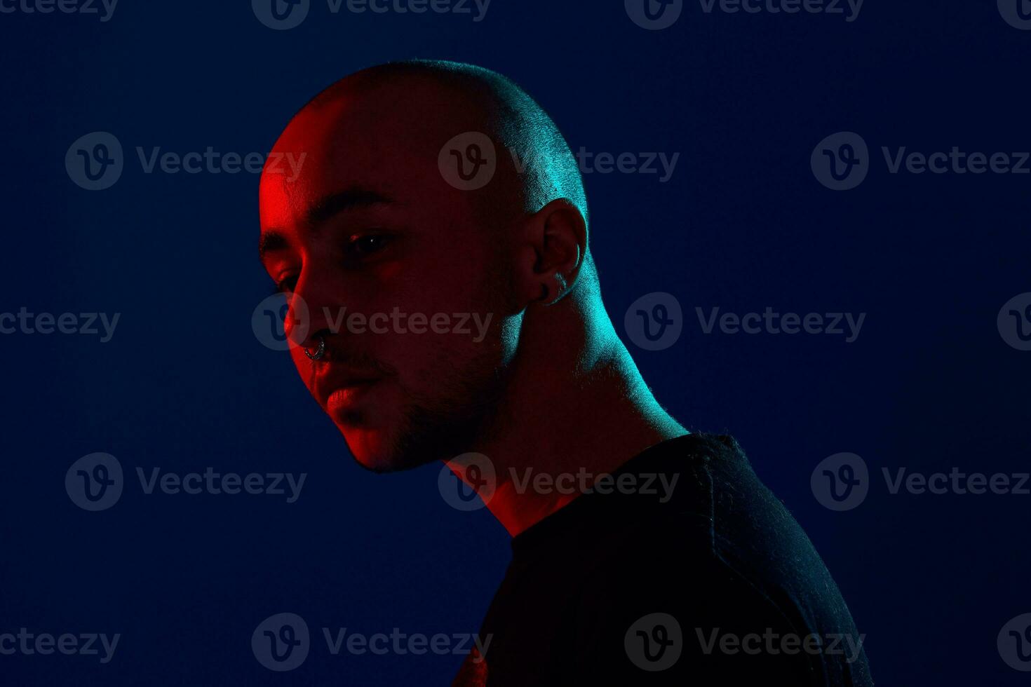 Studio shot of a young tattoed bald man posing against a blue background. 90s style. photo