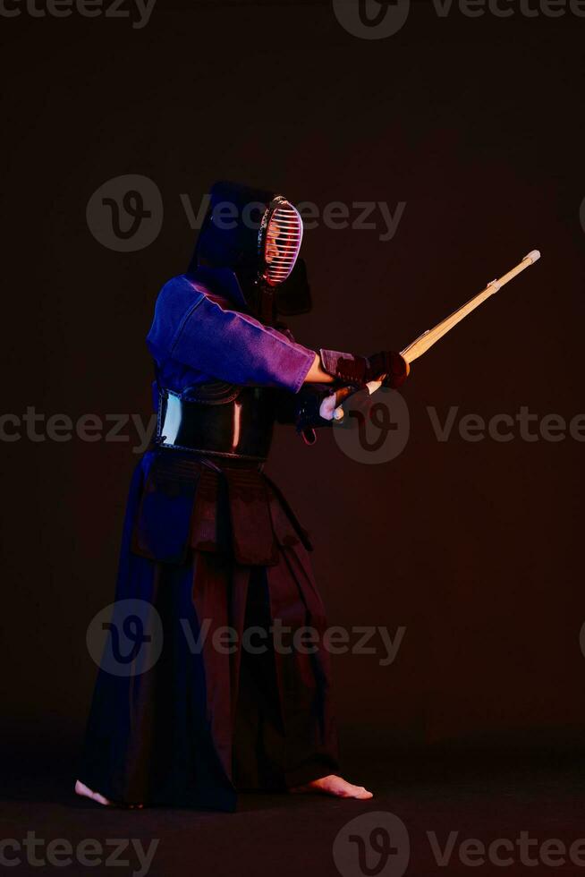 cerca arriba disparo, kendo combatiente vistiendo en un armadura, tradicional kimono, casco practicando marcial Arte con shinai bambú espada, negro antecedentes. foto