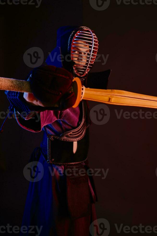 Close up shot, Kendo fighter wearing in an armor, traditional kimono, helmet practicing martial art with shinai bamboo sword, black background. photo