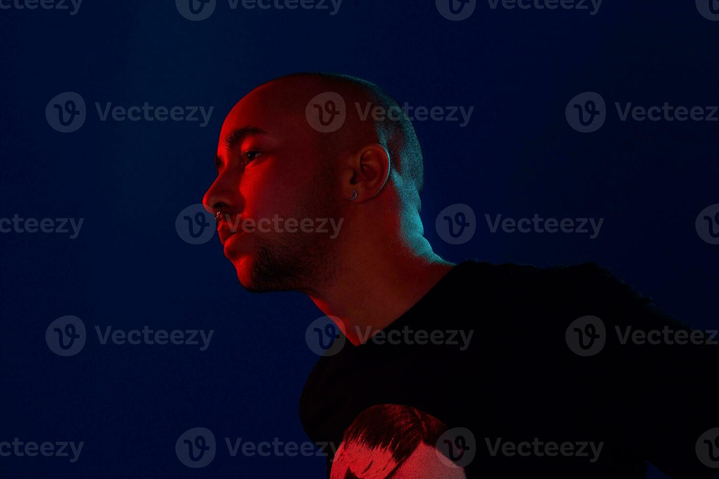 Studio shot of a young tattoed bald man posing against a blue background. 90s style. photo