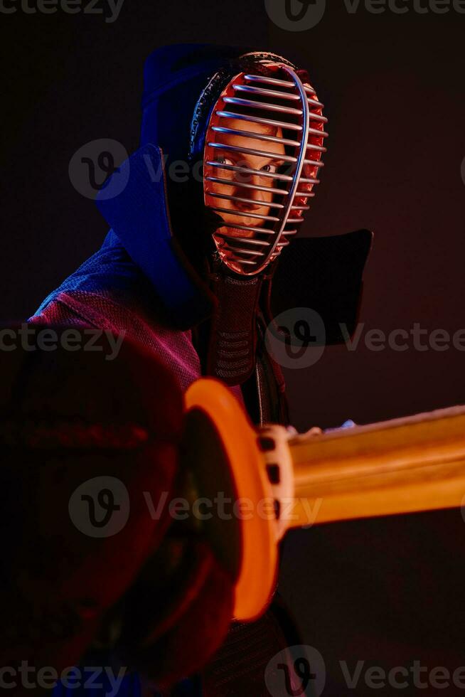 cerca arriba disparo, kendo combatiente vistiendo en un armadura, tradicional kimono, casco practicando marcial Arte con shinai bambú espada, negro antecedentes. foto