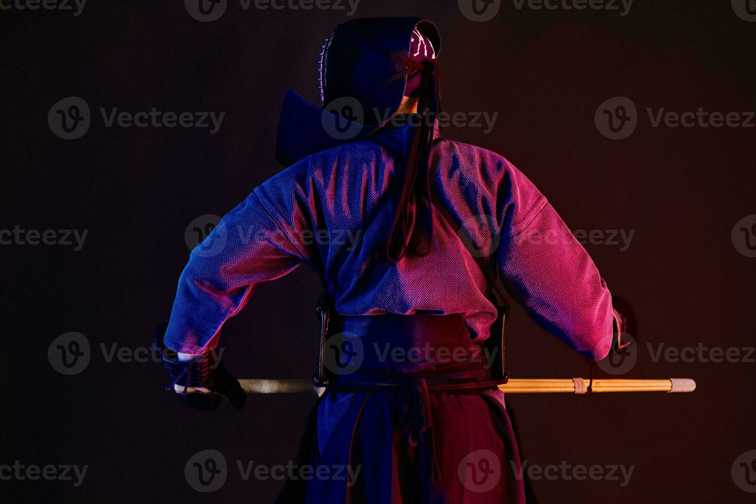 Close up. Kendo fighter wearing in an armor, traditional kimono, helmet practicing martial art, shinai bamboo sword, standing back, black background. photo