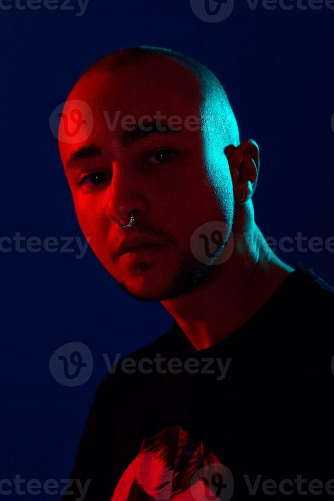 Studio shot of a young tattoed bald man posing against a blue background. 90s style. photo