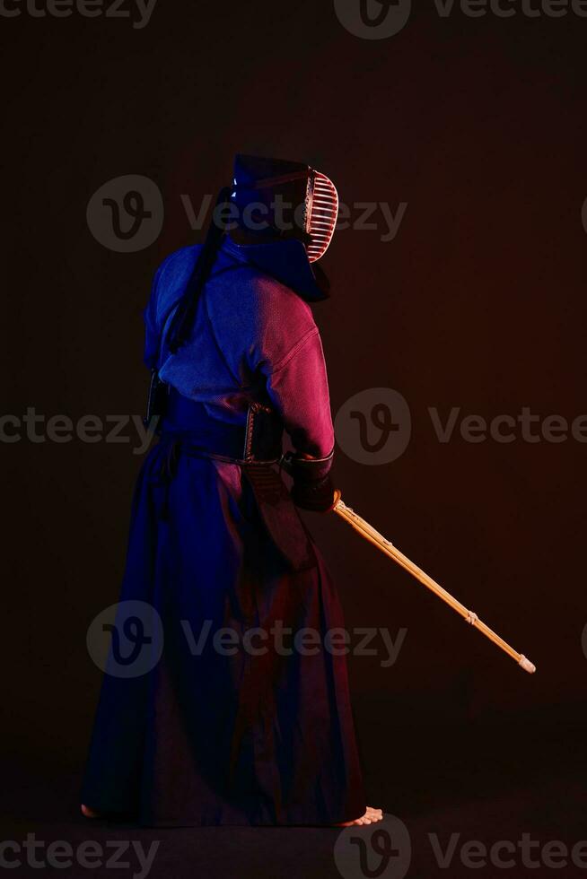 cerca arriba disparo, kendo combatiente vistiendo en un armadura, tradicional kimono, casco practicando marcial Arte con shinai bambú espada, negro antecedentes. foto