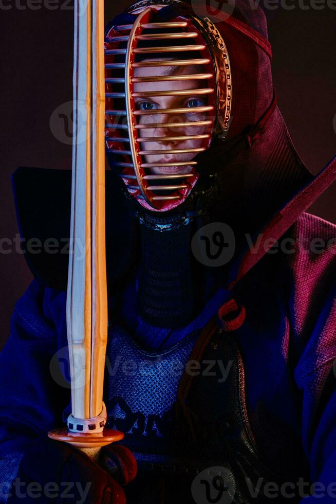 Close up shot, Kendo fighter wearing in an armor, traditional kimono, helmet practicing martial art with shinai bamboo sword, black background. photo