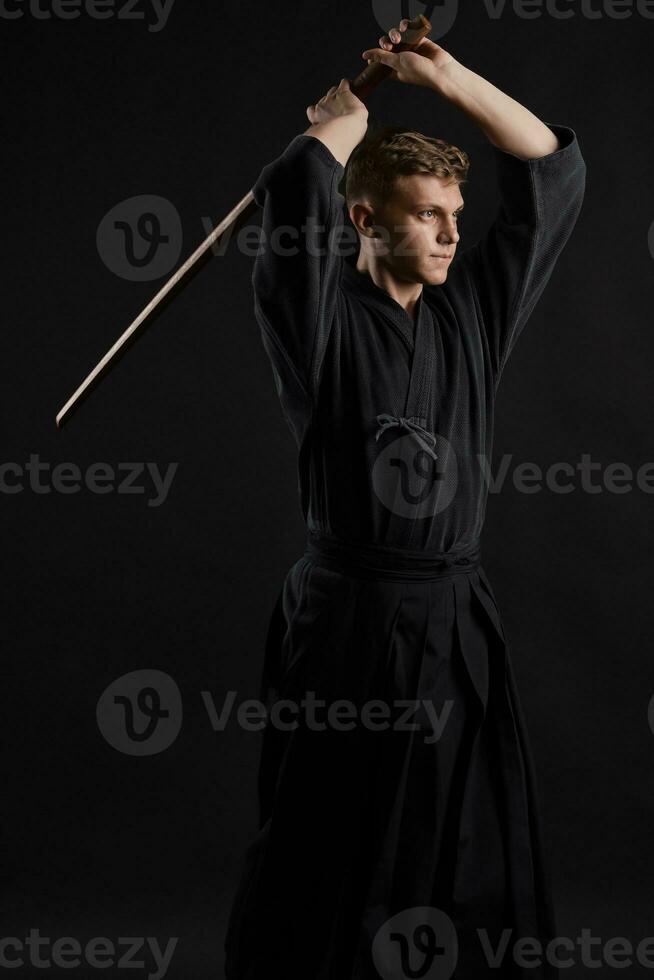 kendo gurú vistiendo en un tradicional japonés kimono es practicando marcial Arte con el shinai bambú espada en contra un negro estudio antecedentes. foto