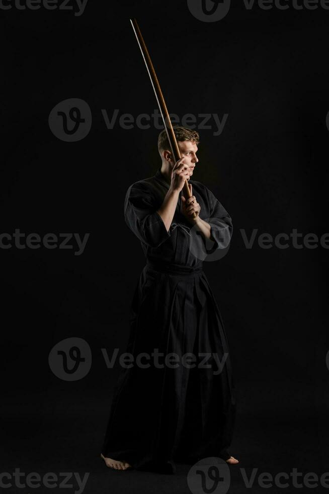 kendo gurú vistiendo en un tradicional japonés kimono es practicando marcial Arte con el shinai bambú espada en contra un negro estudio antecedentes. foto