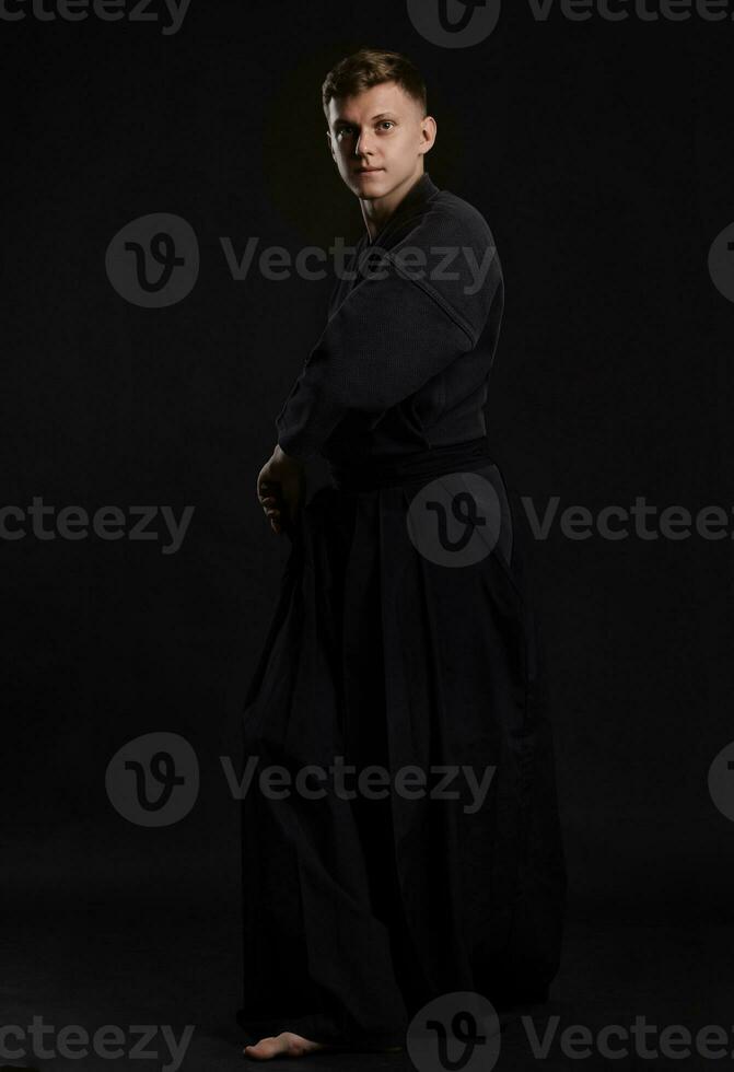 kendo gurú vistiendo en un tradicional japonés kimono es practicando marcial Arte con el shinai bambú espada en contra un negro estudio antecedentes. foto