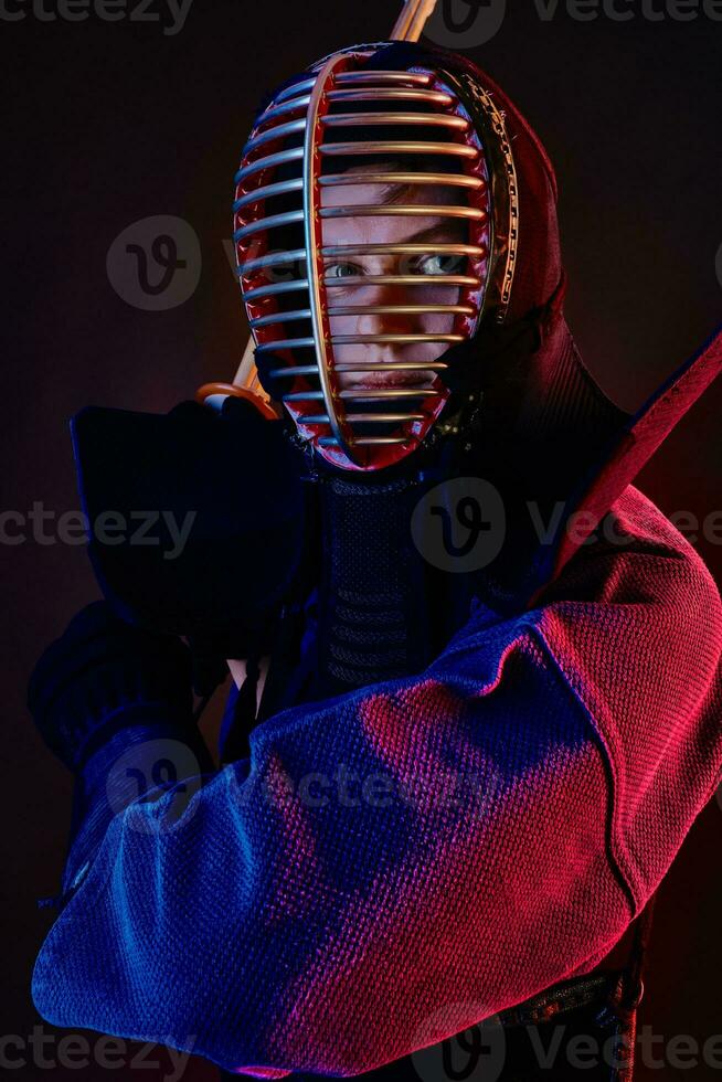 Close up shot, Kendo fighter wearing in an armor, traditional kimono, helmet practicing martial art with shinai bamboo sword, black background. photo