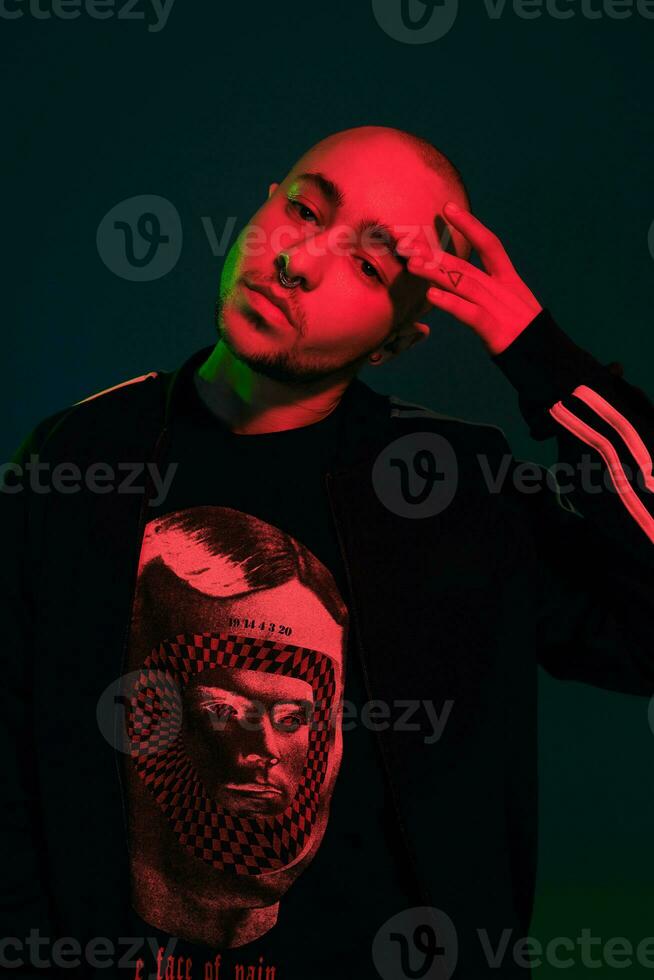 Studio shot of a young tattoed bald man posing against a colorful background. 90s style. photo