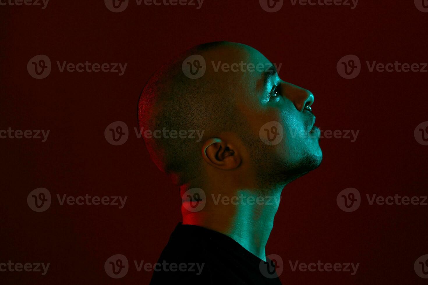 Studio shot of a young tattoed bald man posing against a red background. 90s style. photo