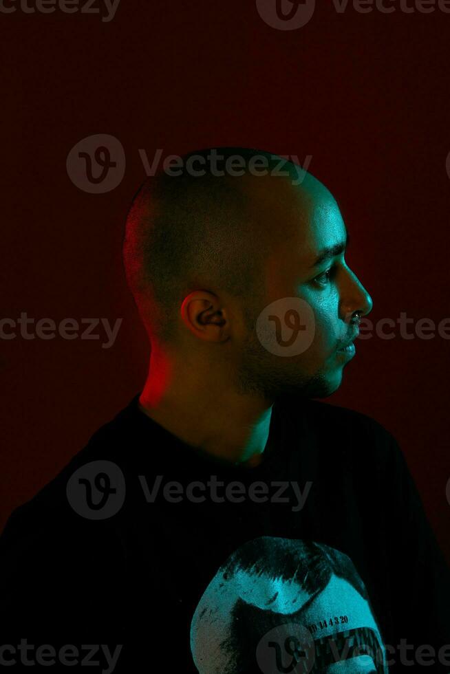 Studio shot of a young tattoed bald man posing against a red background. 90s style. photo