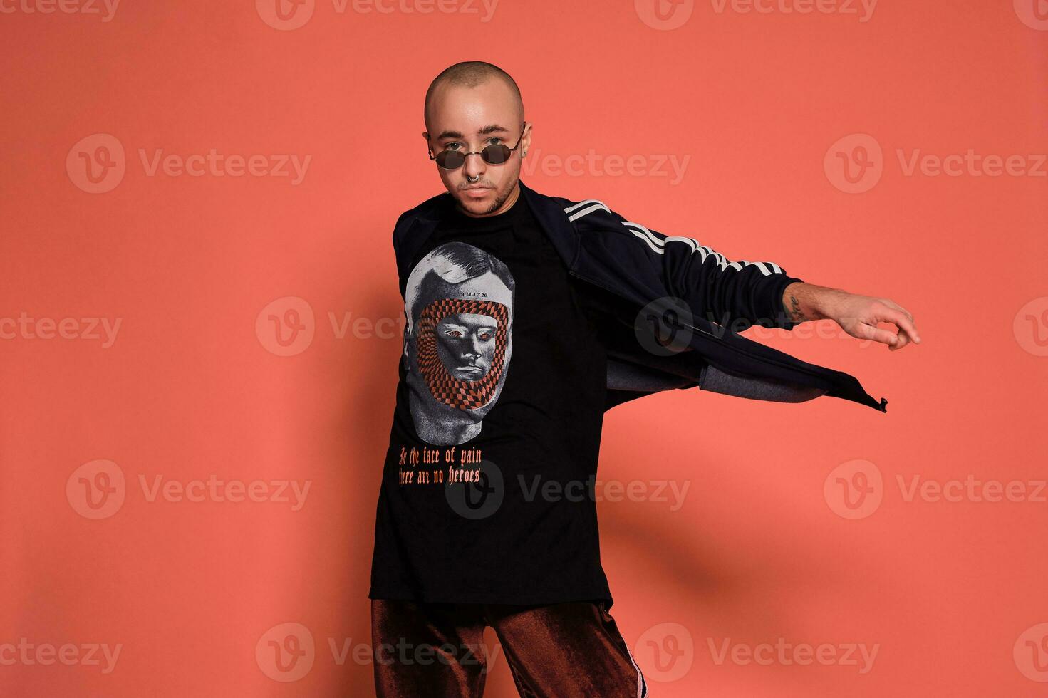 Studio shot of a young tattoed bald man posing against a pink background. 90s style. photo