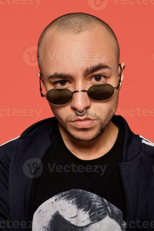 Studio shot of a young tattoed bald man posing against a pink background. 90s style. photo