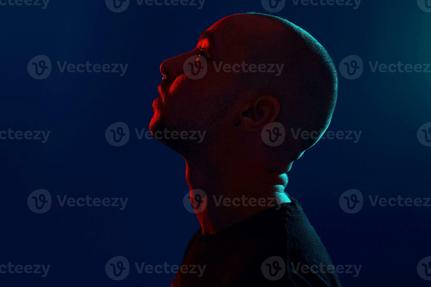 Studio shot of a young tattoed bald man posing against a blue background. 90s style. photo
