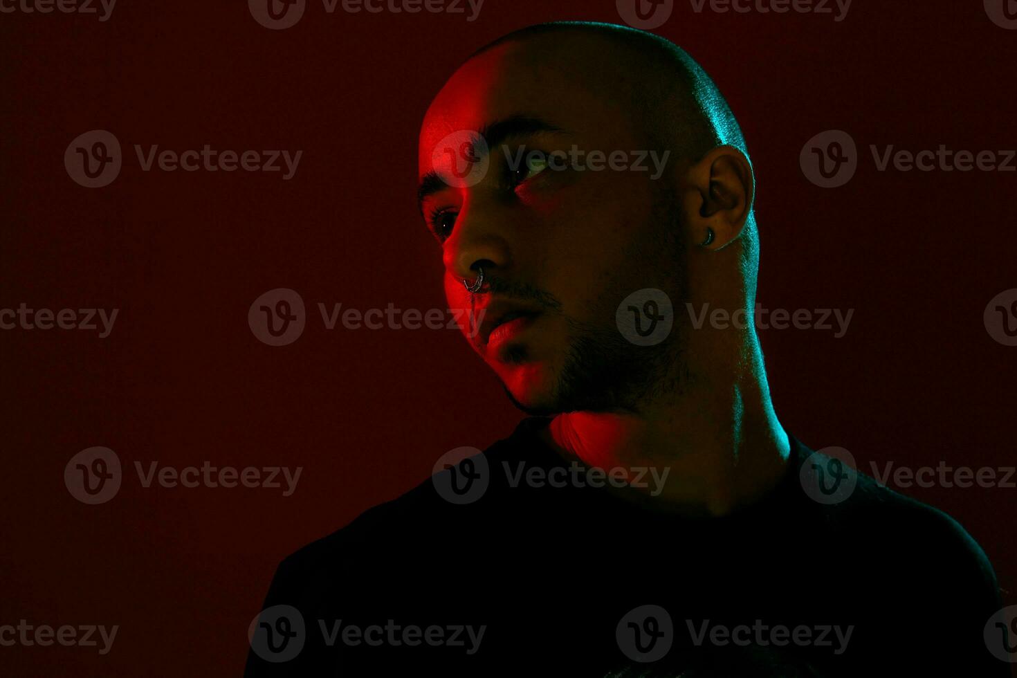 Studio shot of a young tattoed bald man posing against a red background. 90s style. photo