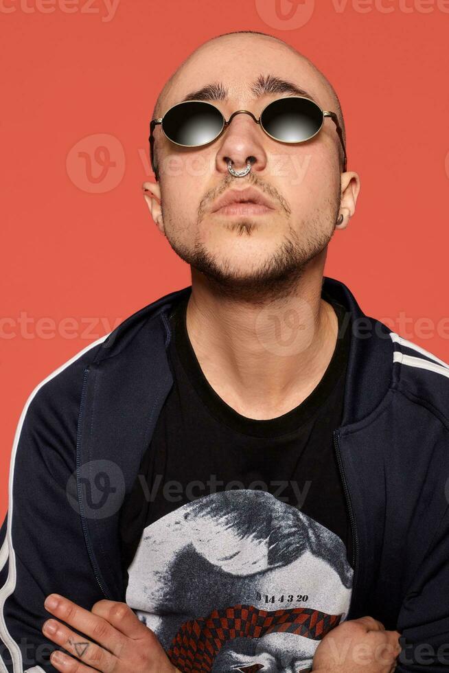 estudio Disparo de un joven tatuado calvo hombre posando en contra un rosado antecedentes. 90s estilo. foto