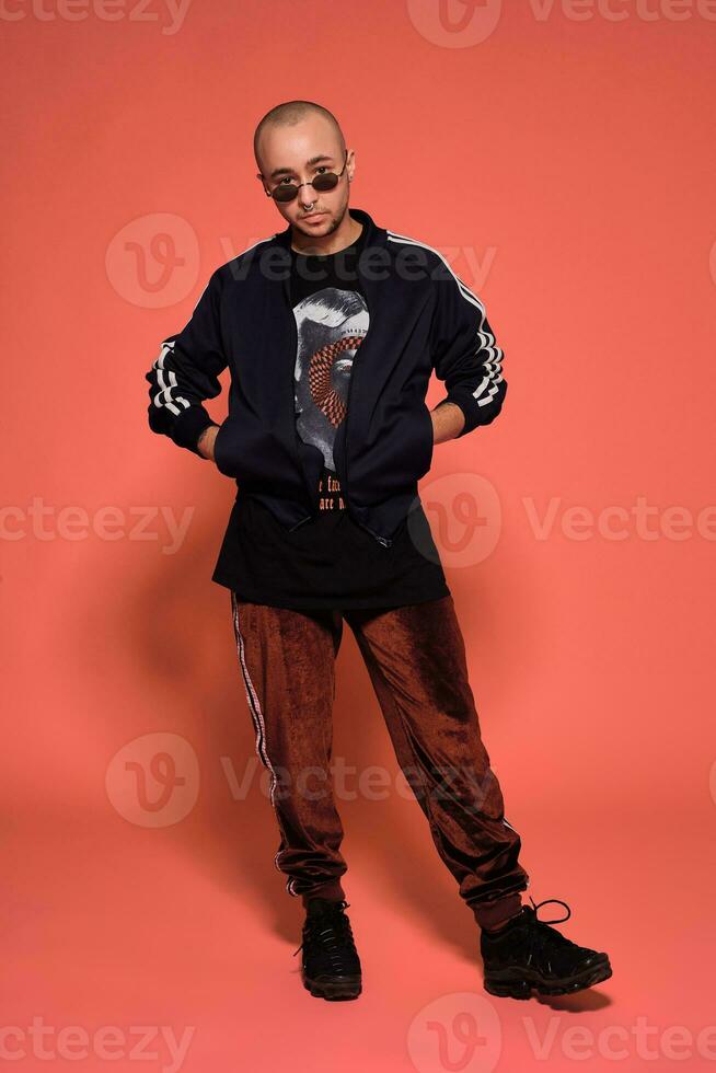 Studio shot of a young tattoed bald man posing against a pink background. 90s style. photo