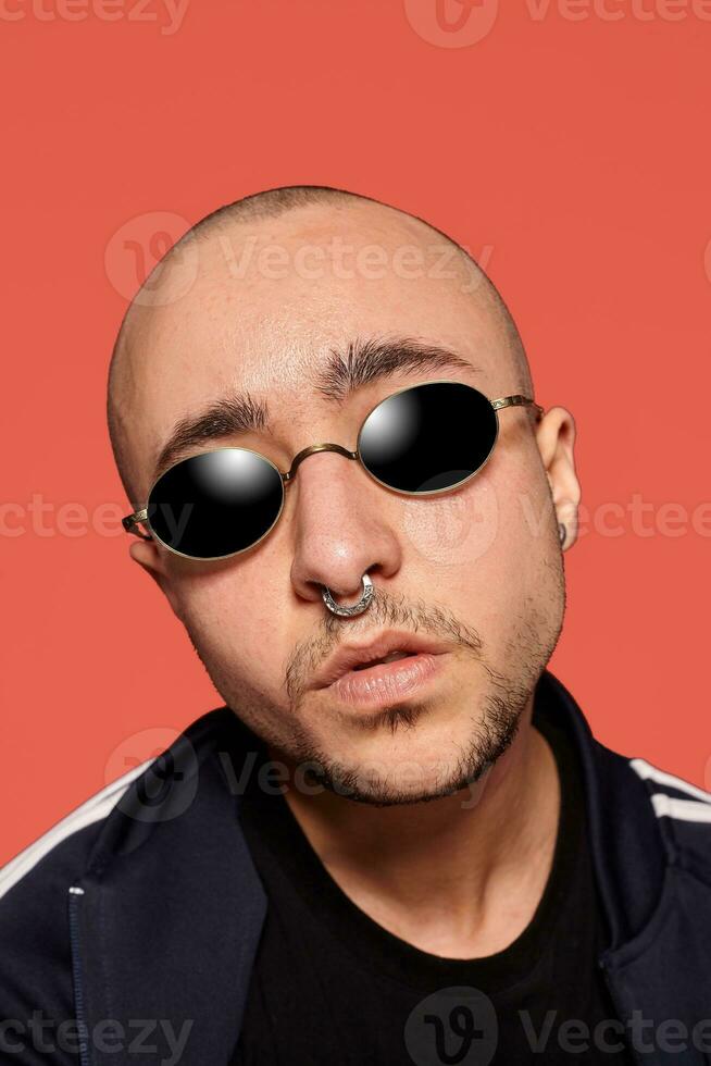 Studio shot of a young tattoed bald man posing against a pink background. 90s style. photo