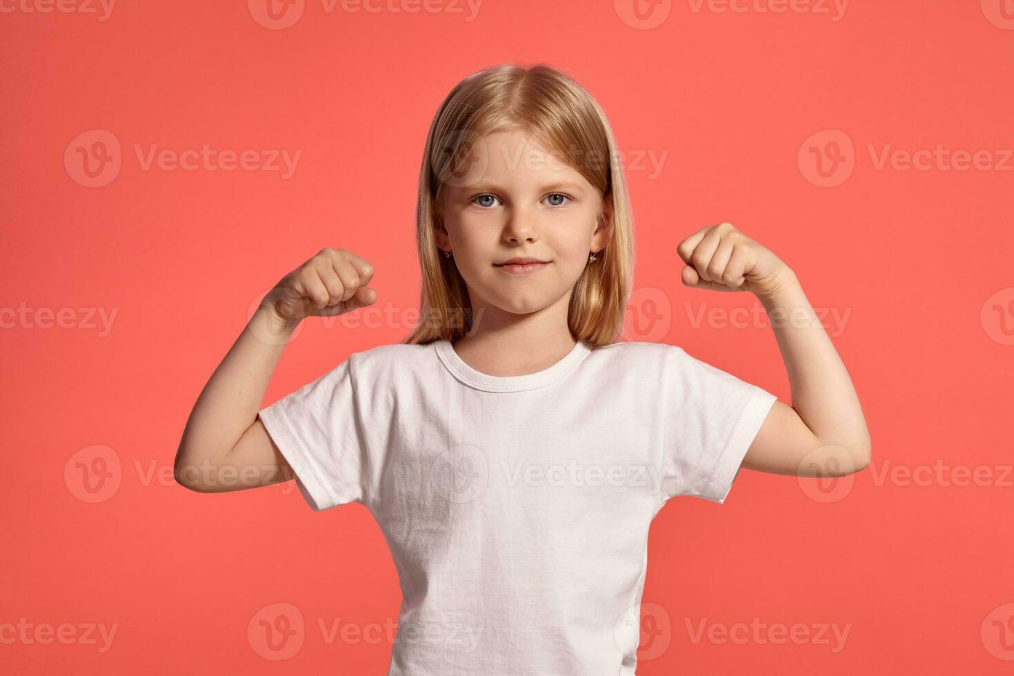 Close-up studio shot of a nice blonde little girl in a white t-shirt posing against a pink background. photo
