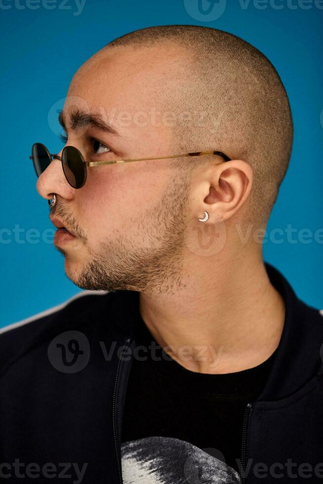 Studio shot of a young tattoed bald man posing against a blue background. 90s style. photo