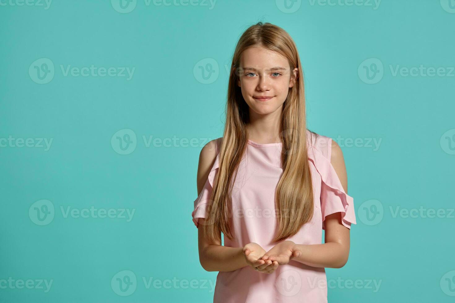 Studio portrait of a beautiful girl blonde teenager in a pink t-shirt posing over a blue background. photo