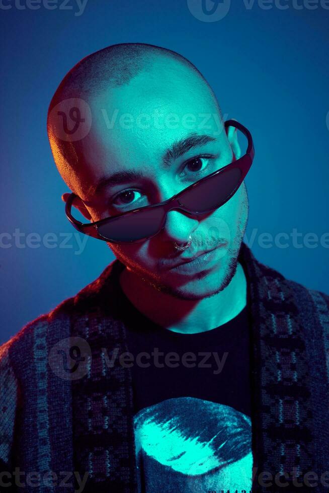 Studio shot of a young tattoed bald man posing against a blue background. 90s style. photo