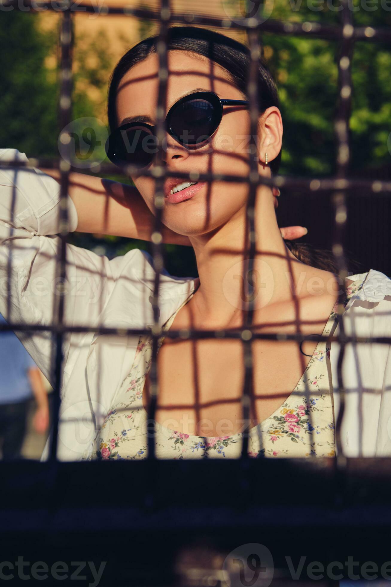portrait-of-girl-in-sunglasses-posing-in-city-behind-a-trellised-fence