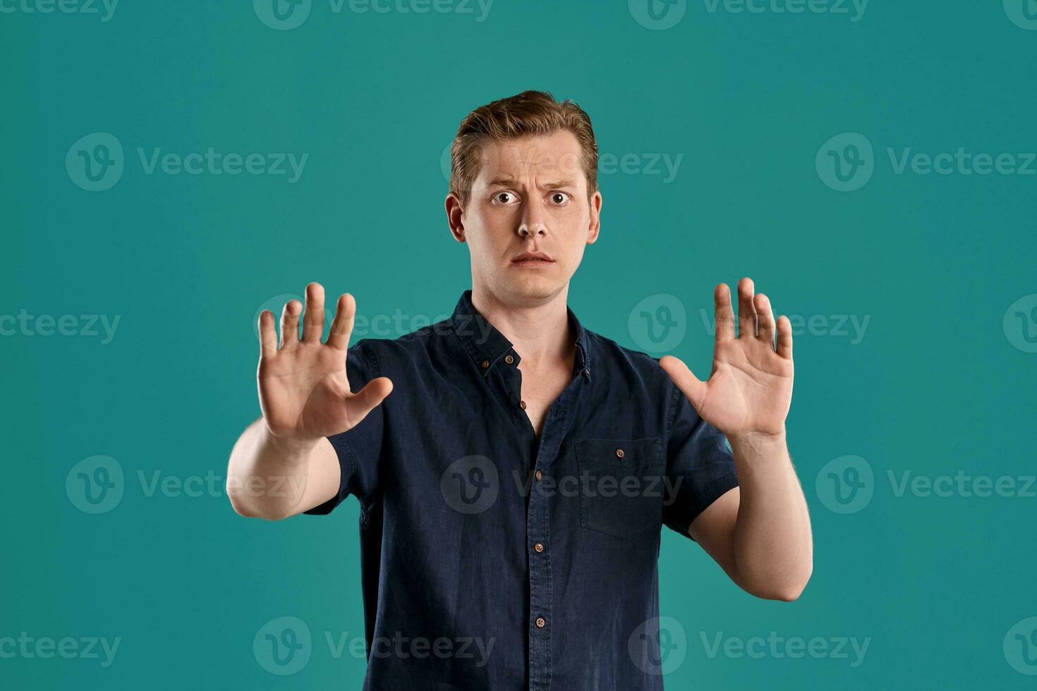 Close-up portrait of a ginger guy in navy t-shirt posing on blue background. Sincere emotions. photo